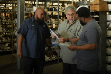 Three Devall Diesel employees looking over paperwork in a warehouse