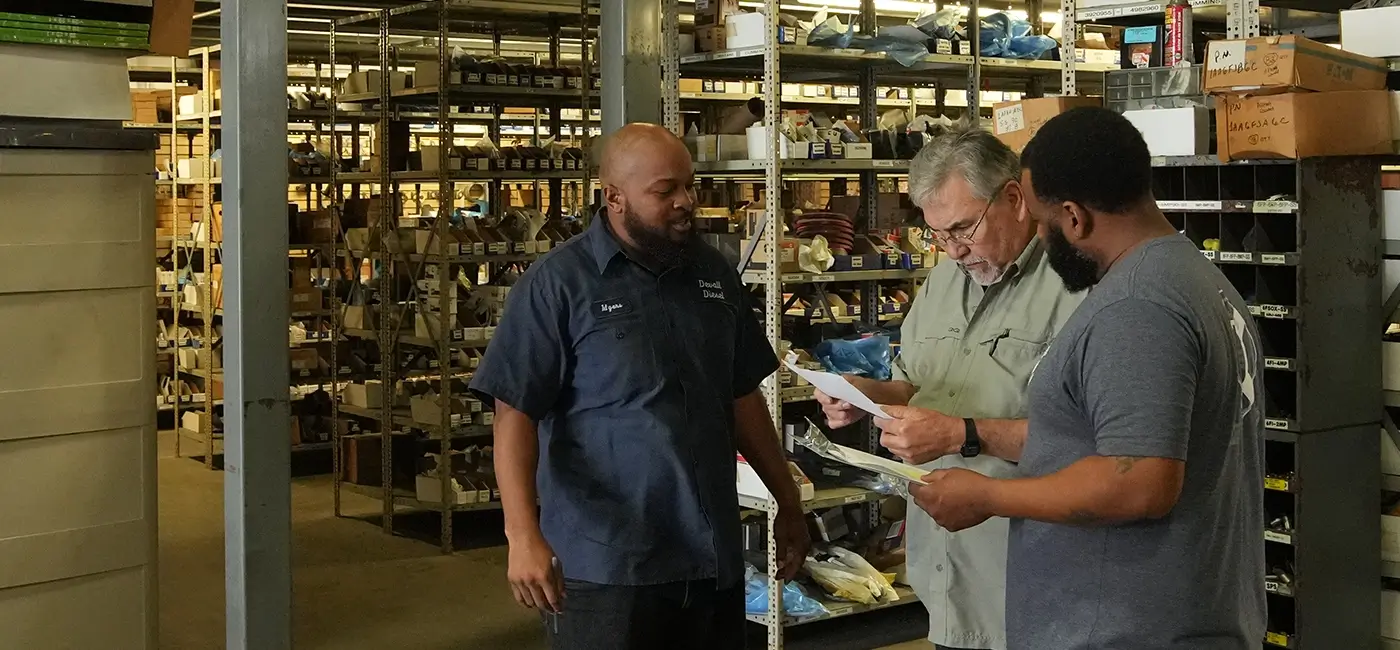 Three Devall Diesel employees looking over paperwork in a warehouse